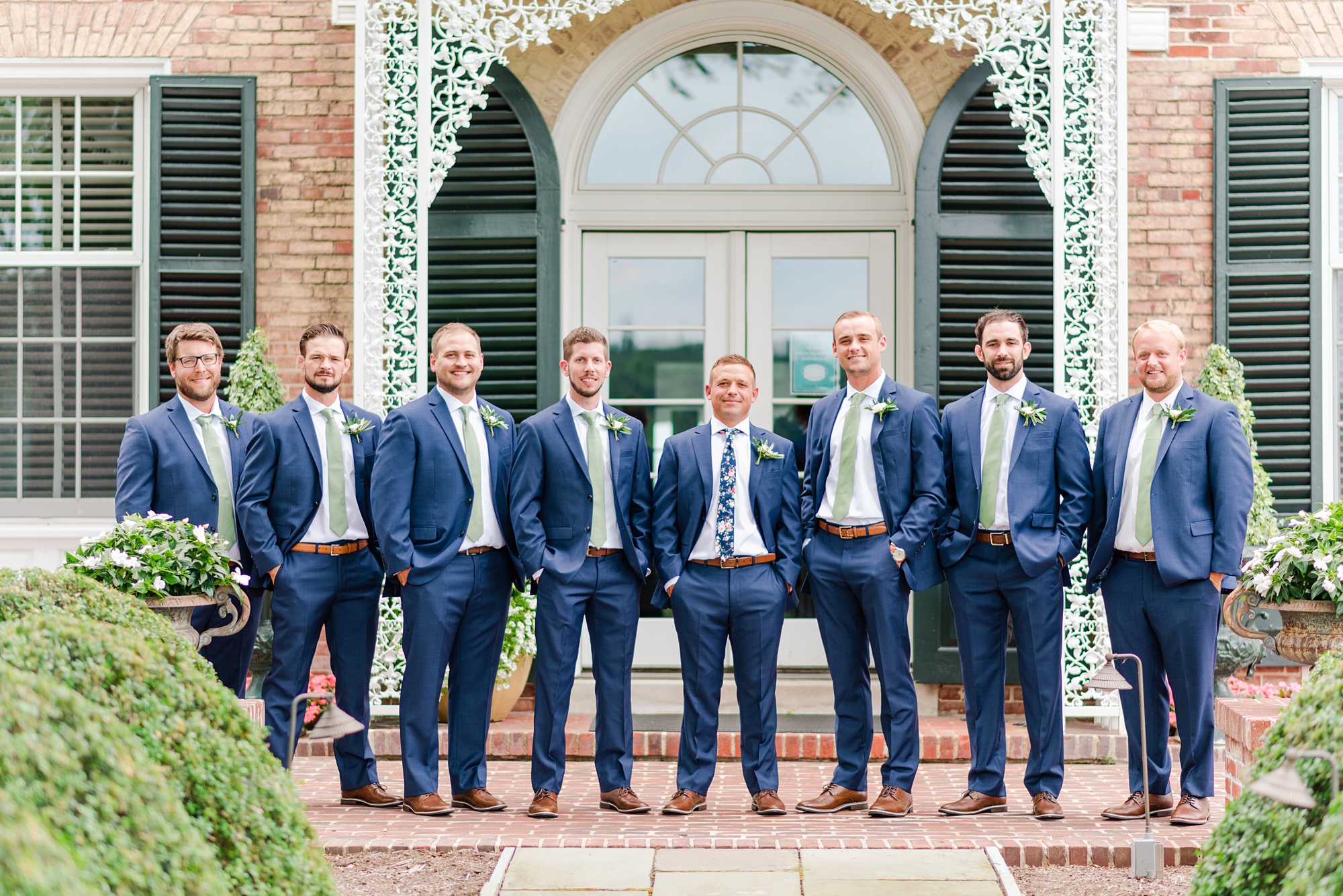 groom and groomsmen in navy suits pose outside house at Drumore Estate