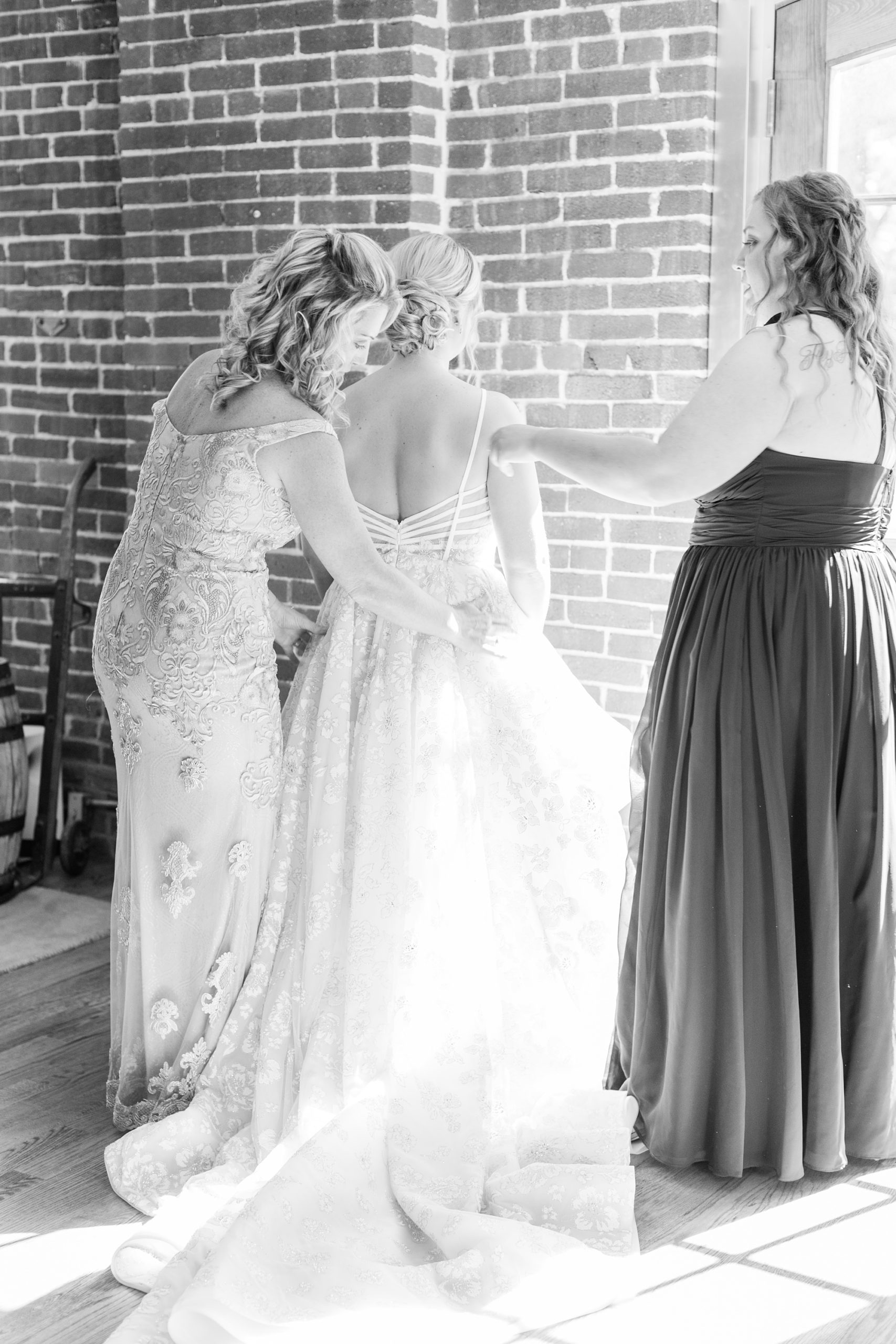 bridesmaids and mother of bride help bride into gown