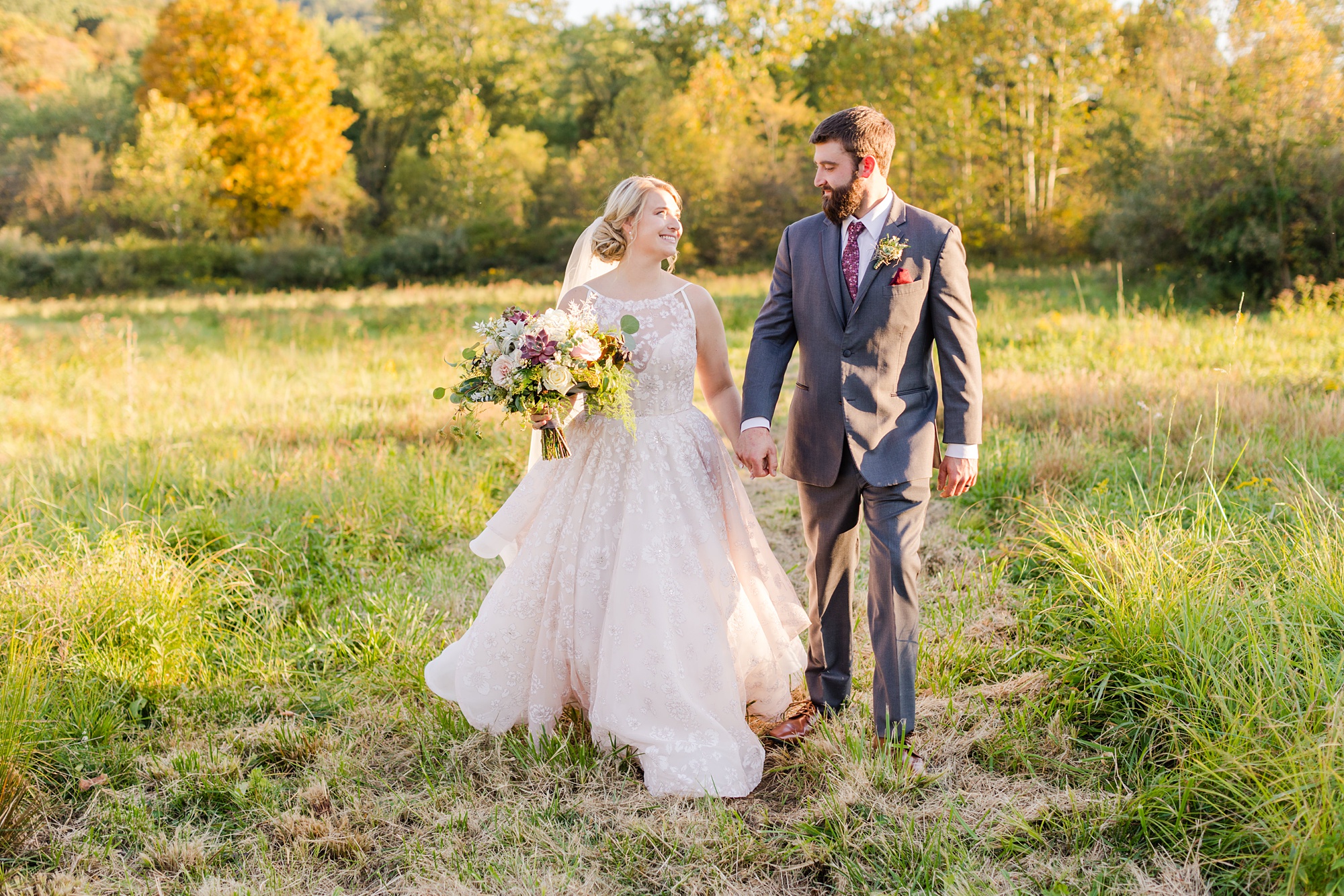 bride and groom hold hands walking through field in PA
